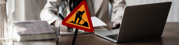 A roadworks sign in front of a person working on a laptop.