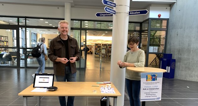 Two researchers are standing behind a table, ready to answer questions. A sign attached to a high table reads "Ask a researcher."