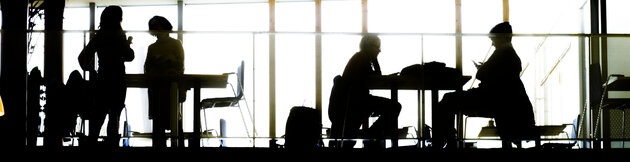 Dark silhouettes of people, tables and chairs against a bright, white sky.