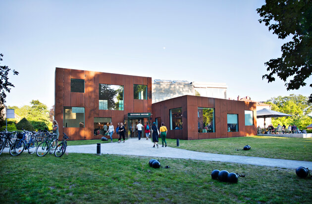 A photo of Skissernas museum against a blue sky. People are walking in and out of the building.